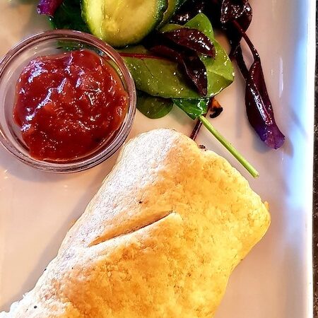 A sausage roll with salad and tomato relish