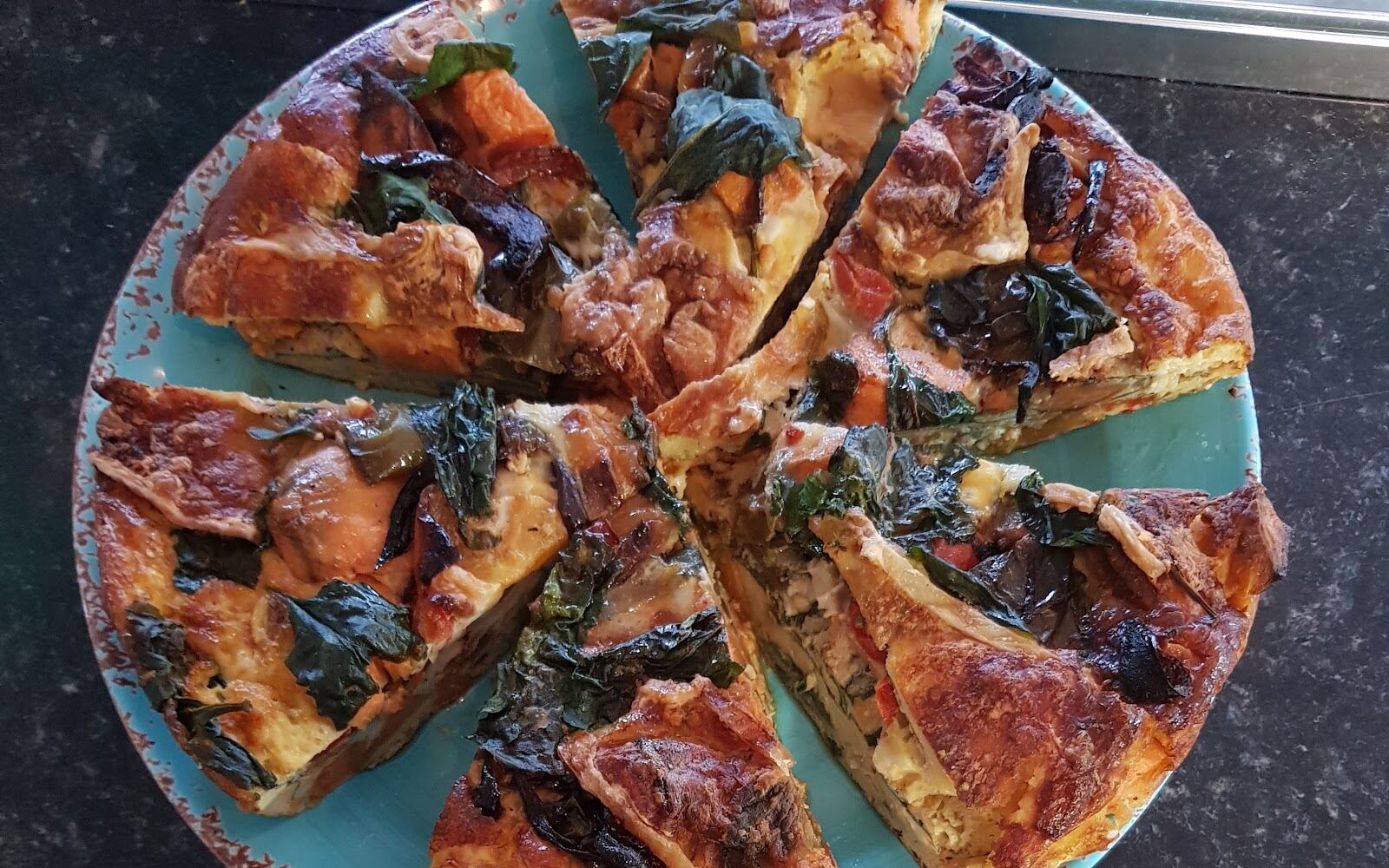 A sliced frittata on a turquoise plate beside a slice with salad