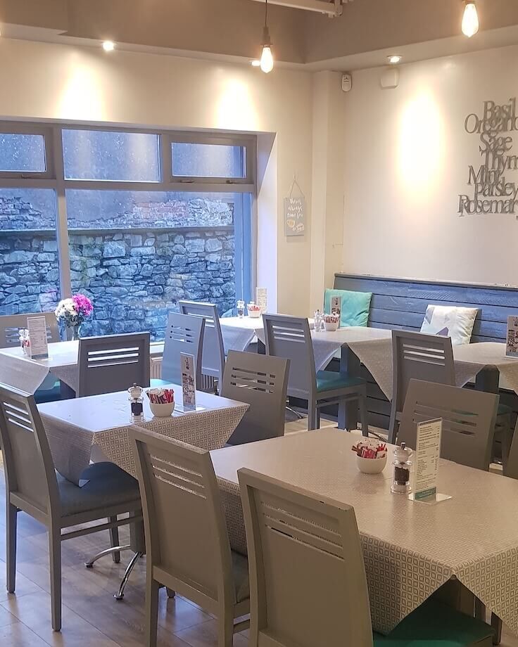 The dining room with grey chairs and tables by a window onto a stone wall